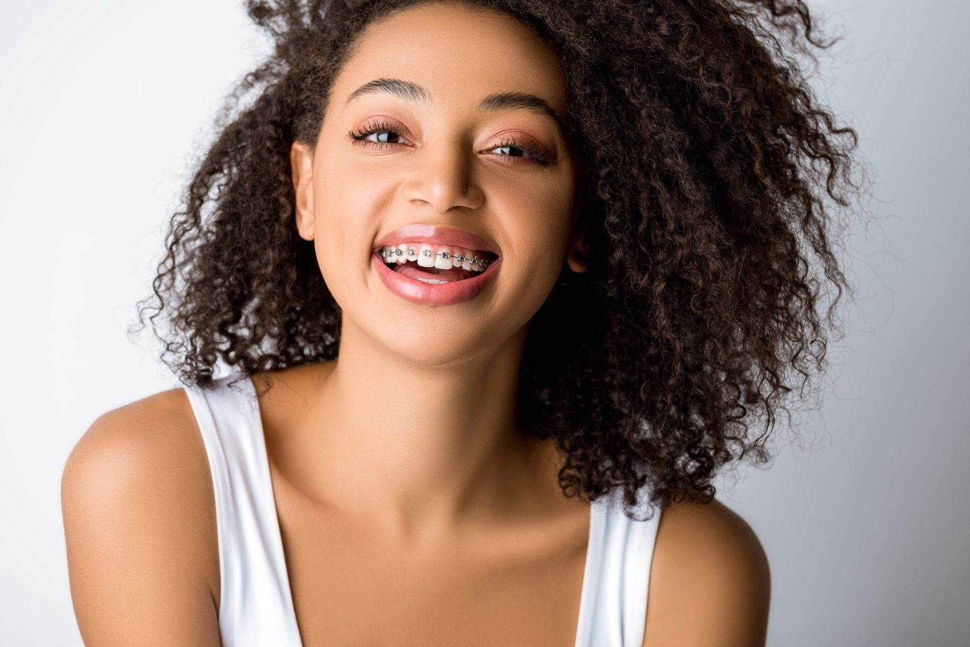 laughing african american girl with dental braces isolated on grey