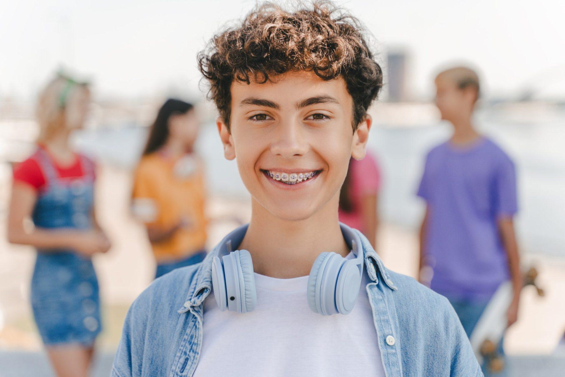 portrait of smiling teenage boy with braces wearing headphones looking at camera on the street