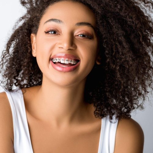 laughing african american girl with dental braces isolated on grey