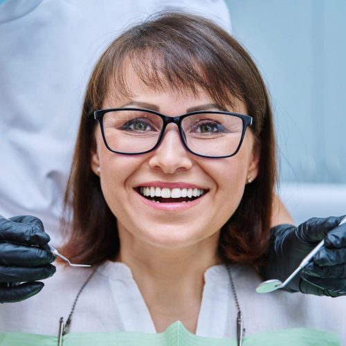 mature woman with teeth in dentistry with hands with dentist examination tools