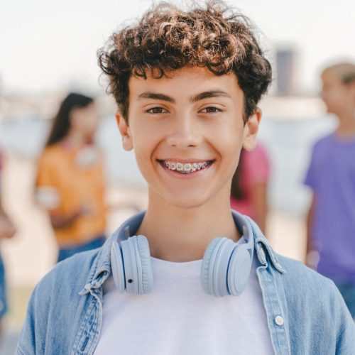 portrait of smiling teenage boy with braces wearing headphones looking at camera on the street