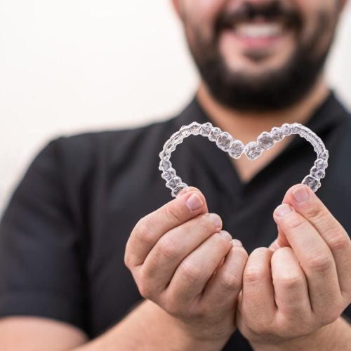 smiling doctor holding heart made of clear aligners for professional teeth correction in clinic